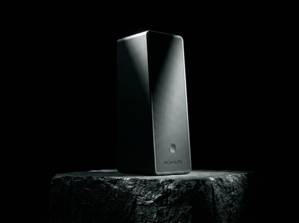 The MONOLITH speaker standing on a plinth, lit like a sculpture.