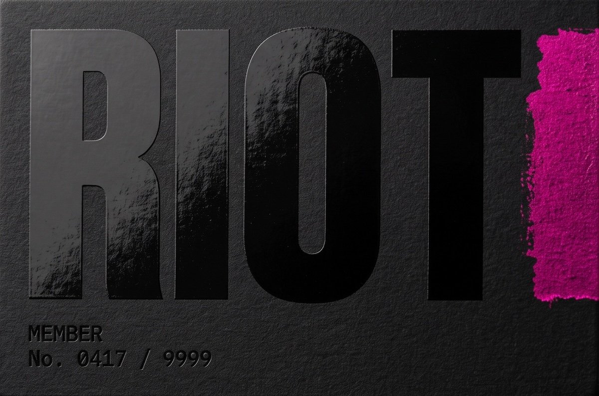 The RIOT loyalty member card — matte black with a screaming pigment swatch and a laser-etched member number.